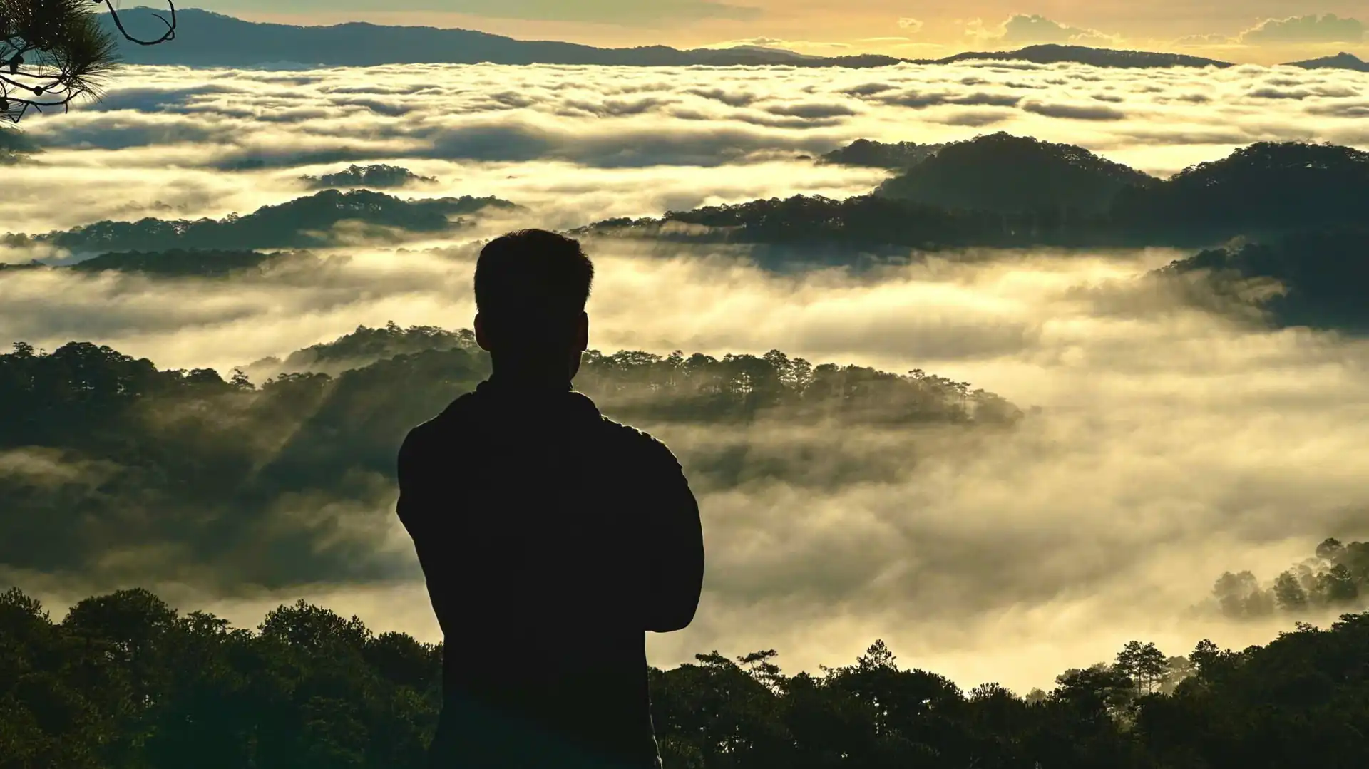 Silhouette of hiker admiring an ocean of white rolling clouds illuminated by sunrise rays from Hon Bo peak in Dalat